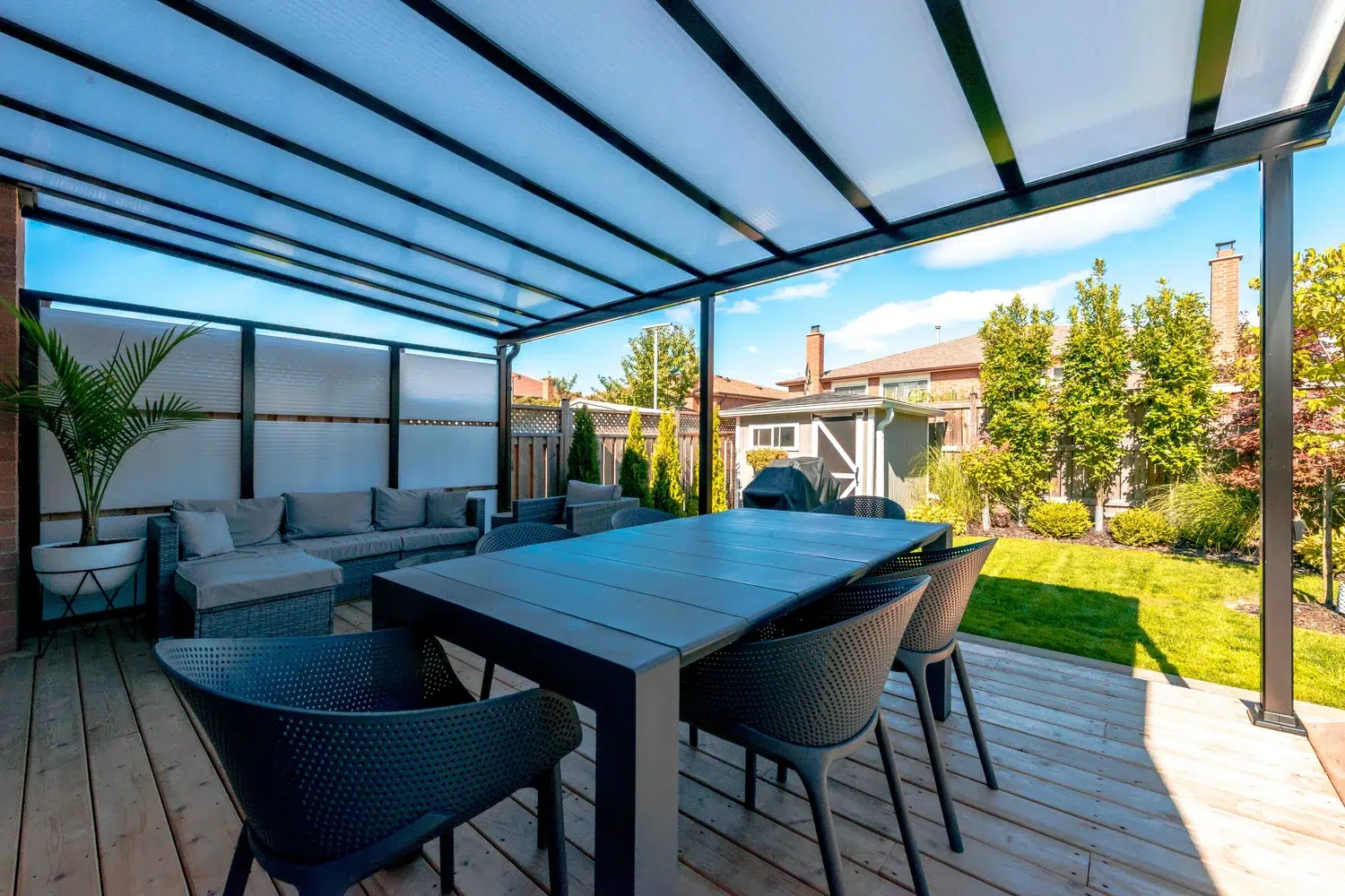 Black-framed acrylic patio cover spreading daylight over an outdoor dining area