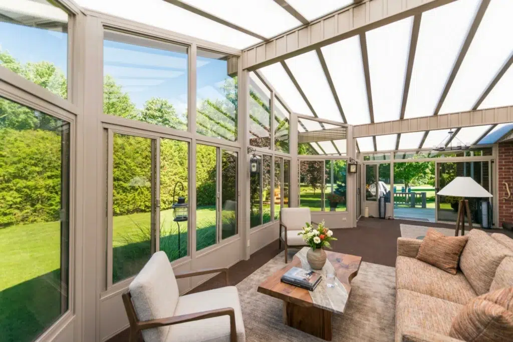 Sunlit glass sunroom with large windows and a bright roof overlooking a green yard