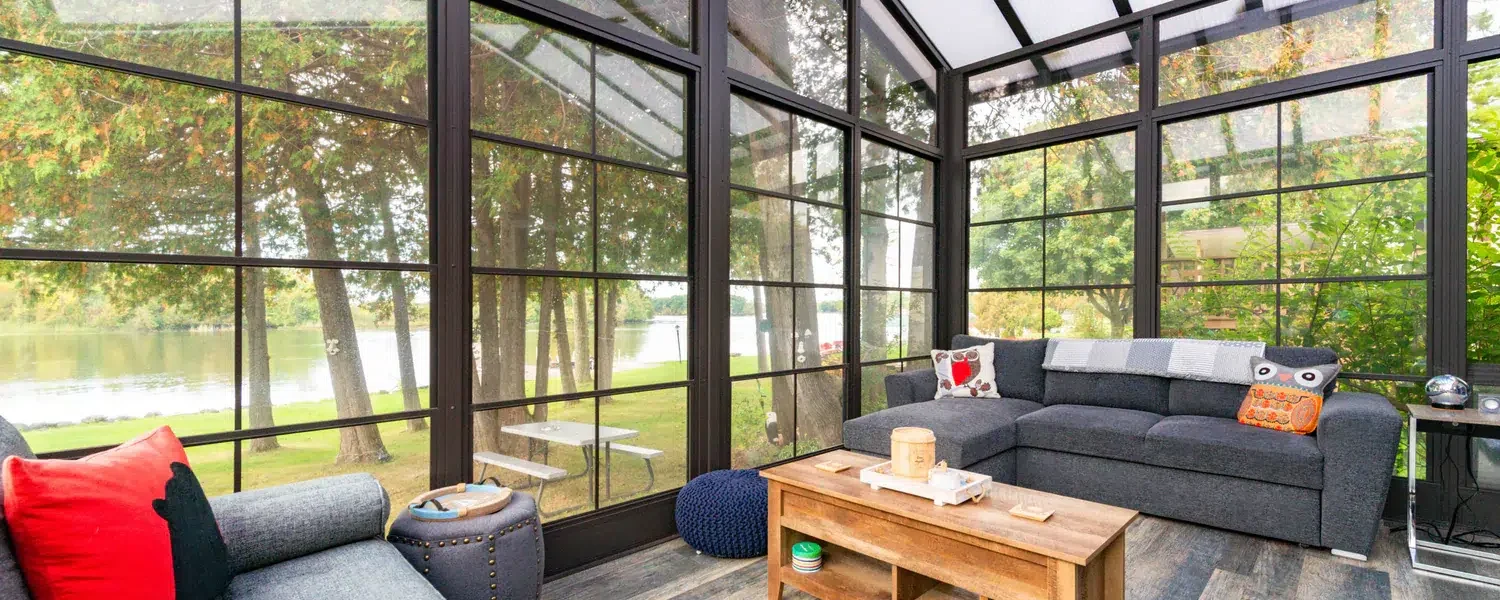 Bright 3-season vinyl sunroom lounge with black frames and a backyard view